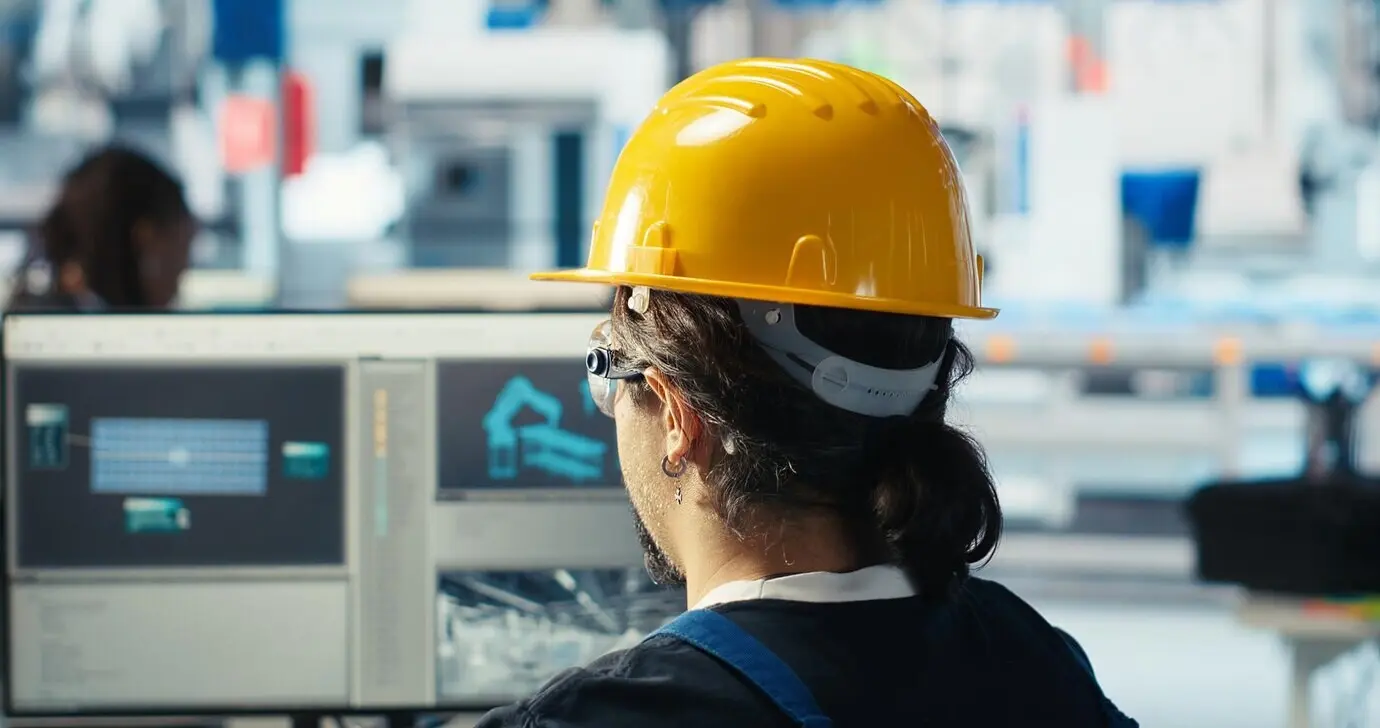 Инженер фотовольтаического завода в жёлтой каске анализирует данные на компьютере.